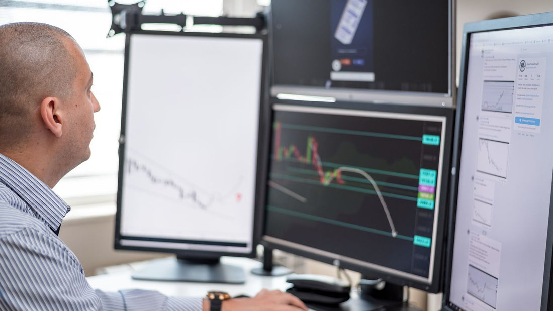 Trader che analizza grafici finanziari su più monitor in una postazione operativa