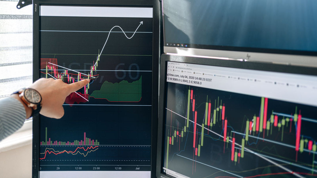 Persona che indica grafici finanziari su due schermi in una postazione di lavoro