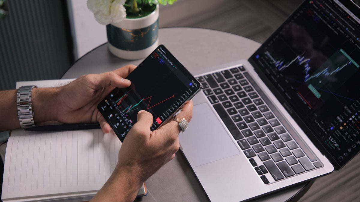Trader al computer e smartphone mentre analizza grafici e operazioni finanziarie