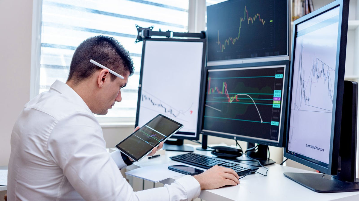 Trader davanti a diversi schermi con grafici dei mercati finanziari