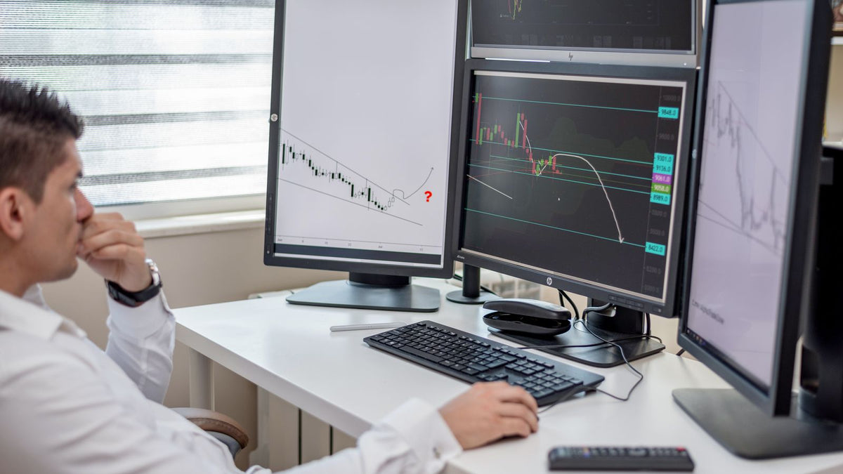 Professionista che studia grafici finanziari su più monitor in una postazione di trading