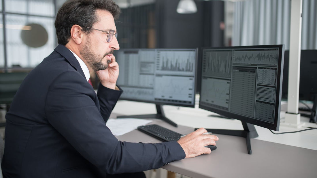 Professionista che consulta i dati di mercato su due monitor in un ufficio