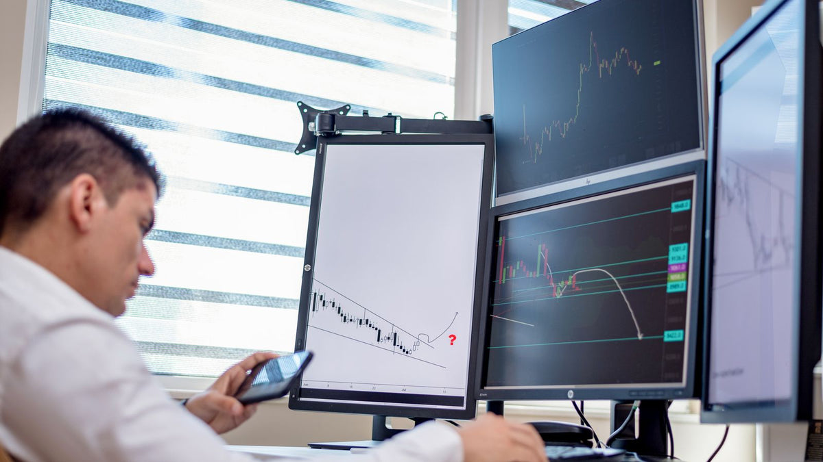 Trader davanti a più monitor con grafici di mercato, attività delle società di prop trading