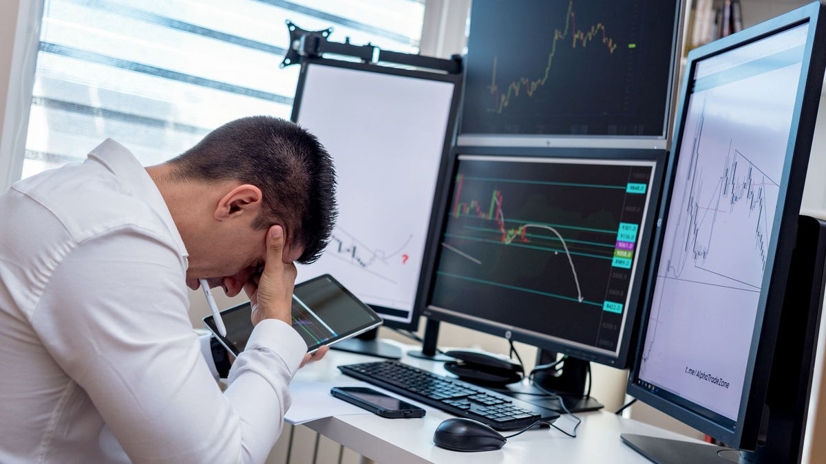Trader preoccupato davanti a più schermi con grafici di mercato, rischio e gestione delle perdite