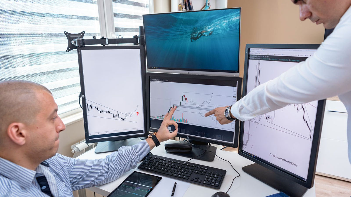 Due professionisti esaminano grafici di mercato su monitor in ufficio, immagine illustrativa